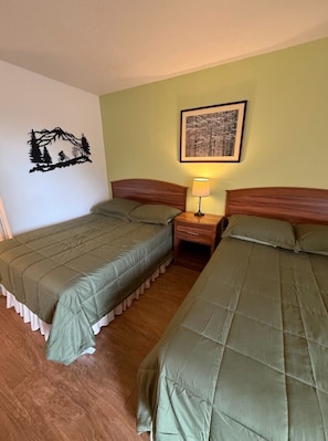 A twin room with two beds, a nightstand, a lamp, and a framed picture on the wall. - Trailhead Lodge (Eureka Springs)