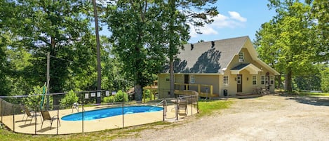 Una casa con piscina, rodeada de árboles y un área cercada.