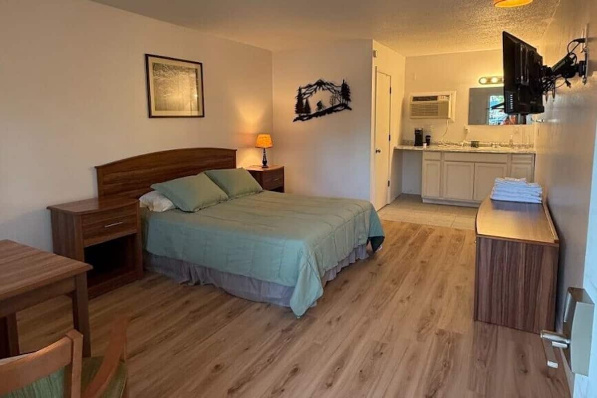 Habitación compacta con cama, mesita de noche, silla y un escritorio pequeño con silla. Cuenta con una kitchenette equipada con pileta, cocina y alacenas.