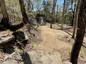 A forested area with a dirt path leading to a large rock formation. - Trailhead Lodge (Eureka Springs)
