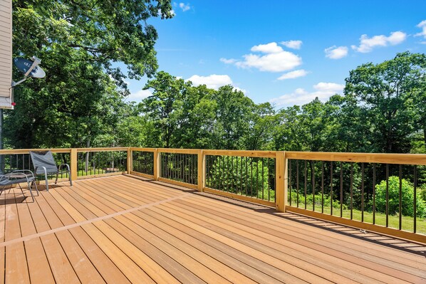 Una terraza de madera con barandilla, rodeada de árboles y un cielo despejado.