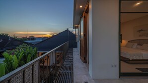 A modern building with a balcony overlooking a residential area, a bedroom with a bed and a wall-mounted artwork, and a clear sky at dusk. - Boutique 4BR Villa With Private Pool & Balcony Suite (Kuta Utara)