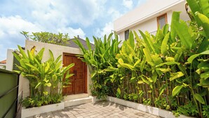 A modern house with a tiled patio, a wooden door, and lush greenery. - Boutique 4BR Villa With Private Pool & Balcony Suite (Kuta Utara)