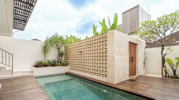 A swimming pool with a wooden deck, a wall with a lattice design, and tropical plants. - Boutique 4BR Villa With Private Pool & Balcony Suite (Kuta Utara)