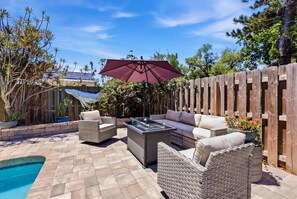 Eine Terrasse im Freien mit Korbmöbeln, einem Tisch mit Glasplatte und einem Pool.