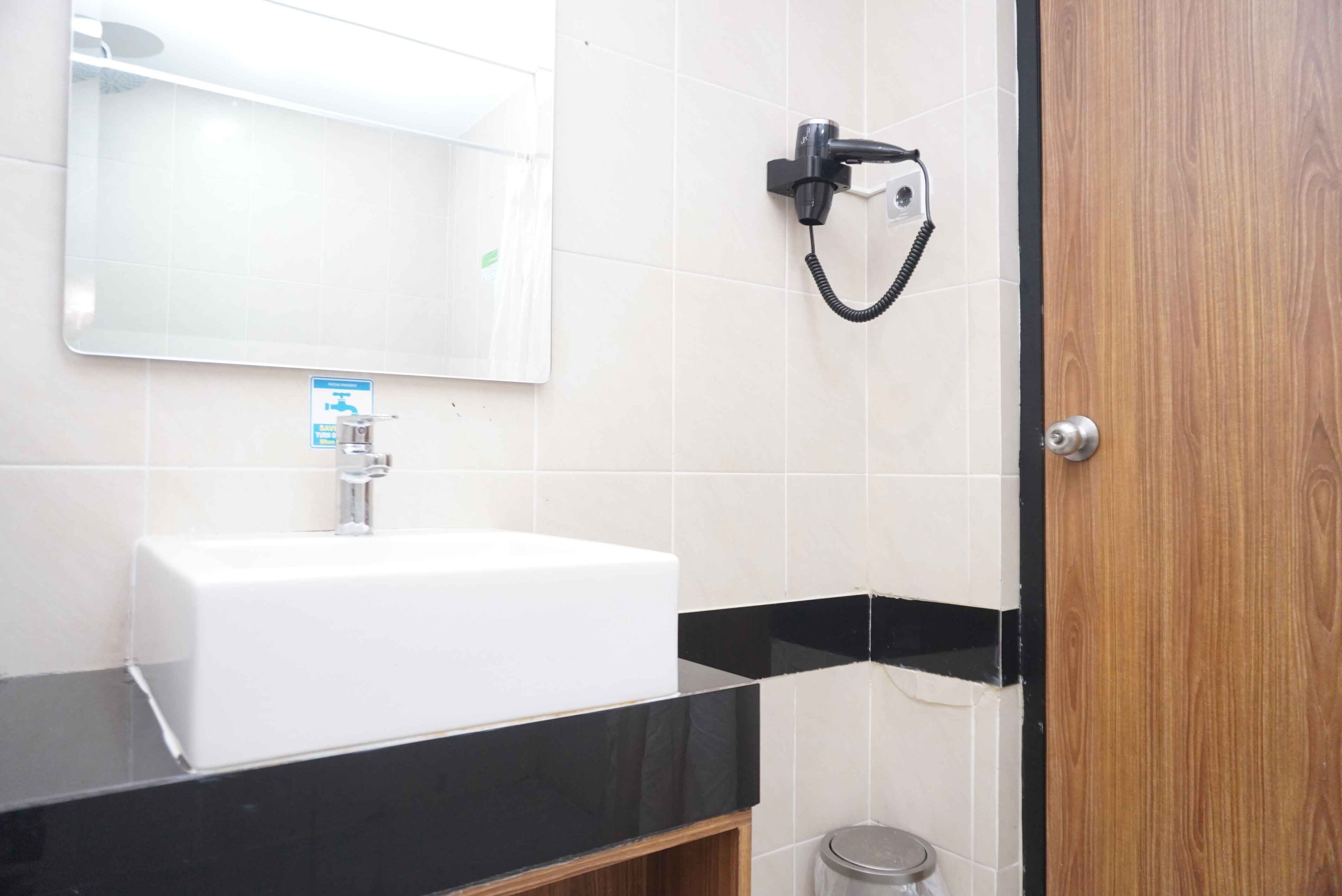 Un baño con un lavamanos blanco, un espejo, un perchero negro y una puerta de madera.