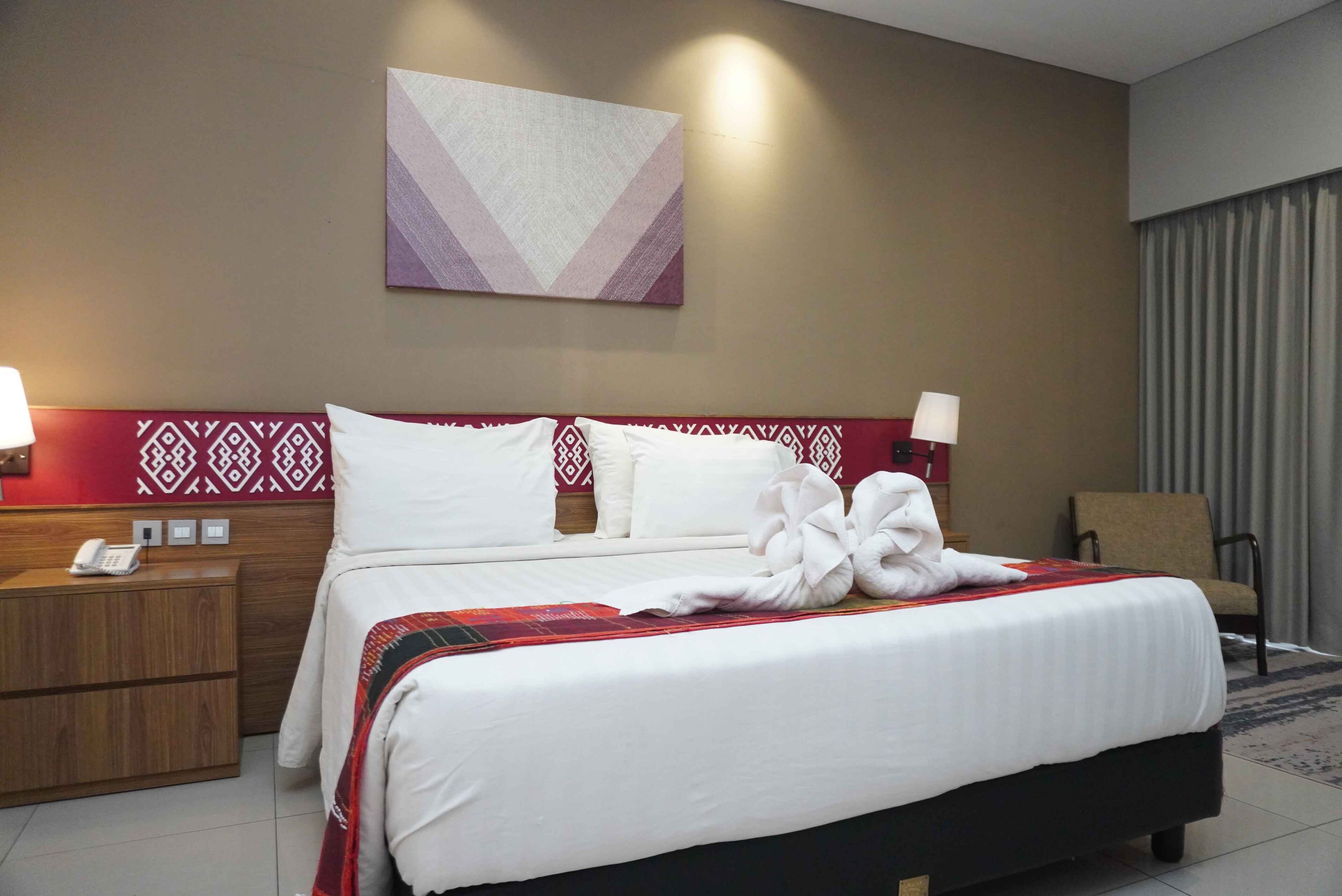 A hotel room with a bed, bedside tables, a wall-mounted artwork, and a chair.
