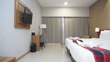Habitación de hotel con cama, escritorio, silla, televisor montado en la pared y ventana con cortinas.