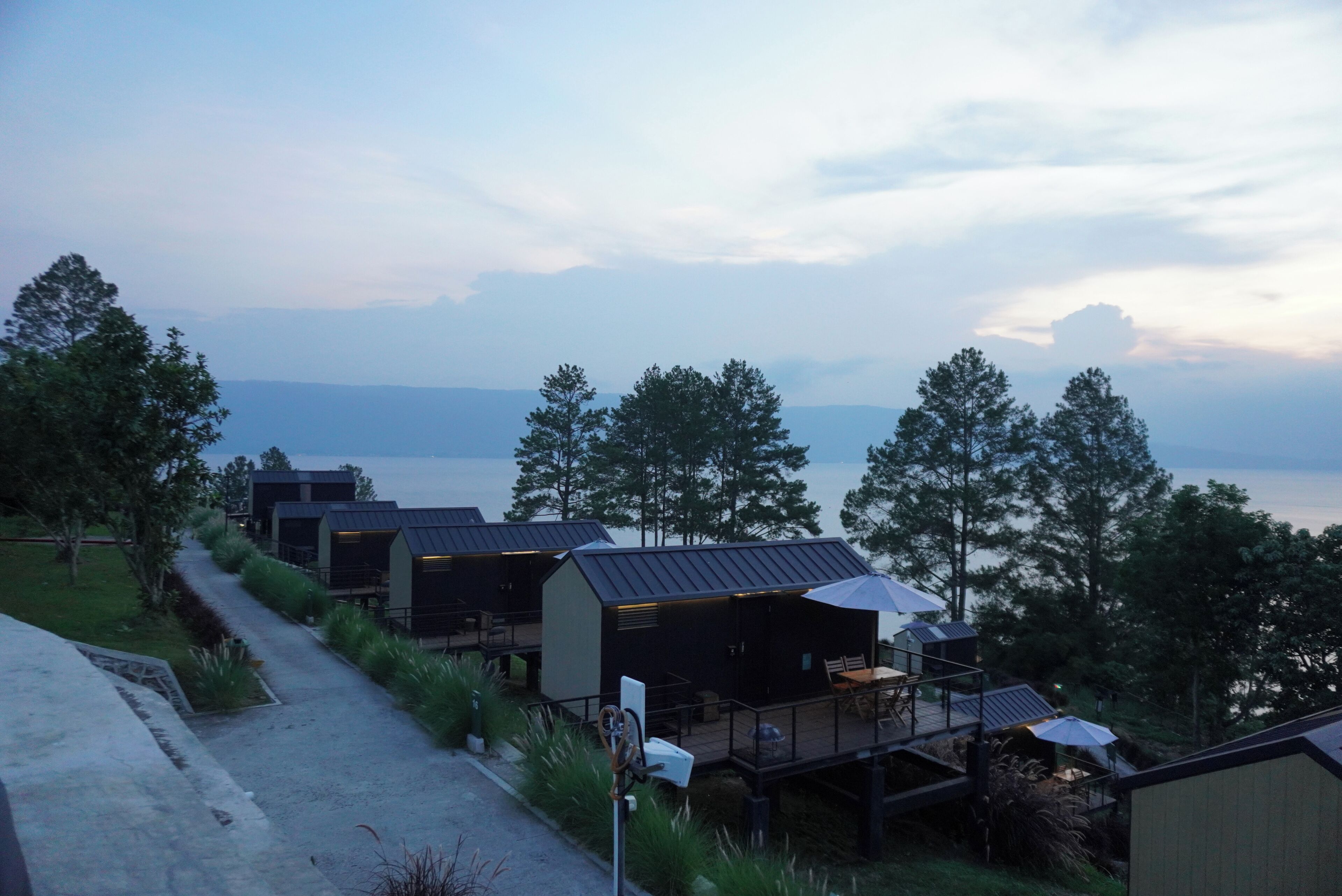 A row of cabins with a deck and outdoor seating, surrounded by trees and a view of the water.