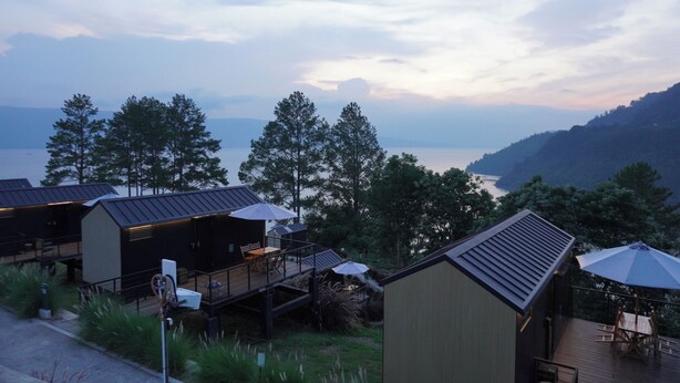 A modern cabin-style hotel with outdoor seating and a view of a lake. - Patra Parapat Hotel (Parapat)
