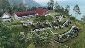 An aerial view of a resort with a large building, multiple cabins, and a scenic mountain backdrop. - Patra Parapat Hotel (Parapat)
