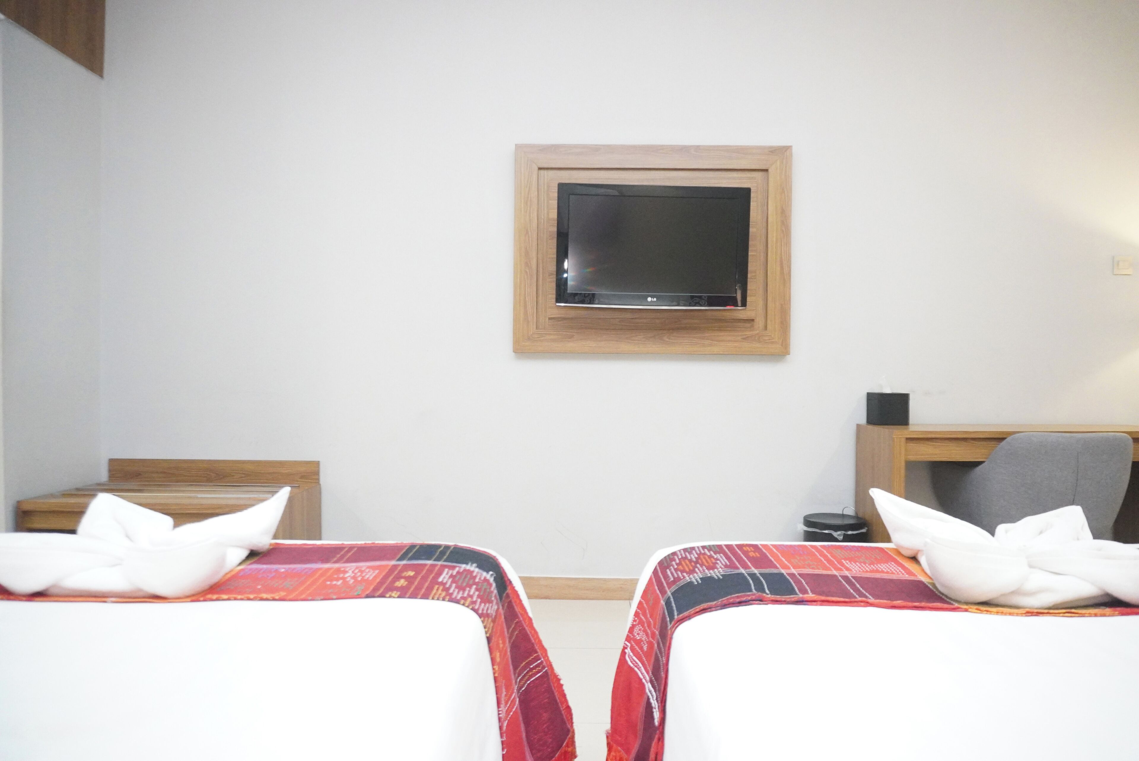 A hotel room with two beds, a TV mounted on the wall, and a desk with a chair.