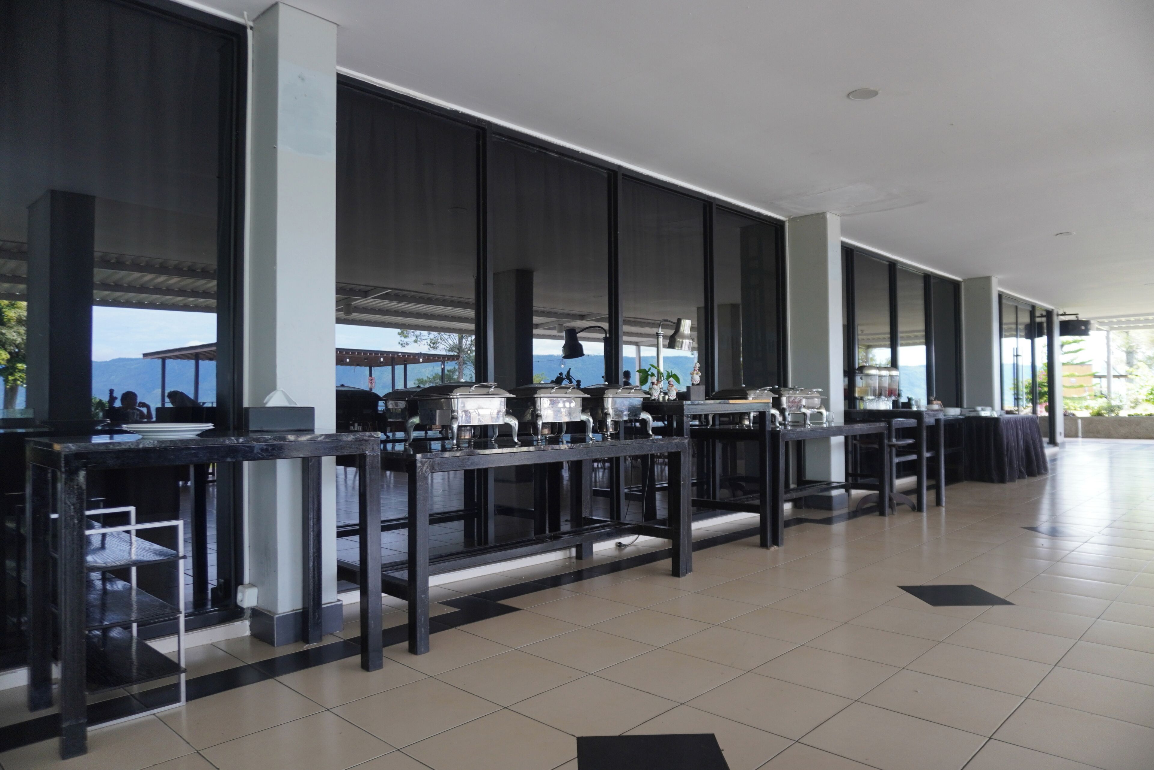 A spacious outdoor dining area with multiple tables and chairs, large windows, and a view of the mountains.