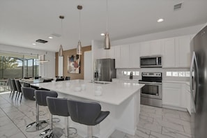 A modern kitchen with white cabinets, stainless steel appliances, and a large island with bar stools. - Privacy Pool-Big Screen! Resort 8 mi 2 Disney-2613 (Kissimmee)