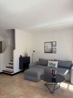 Ein modernes Wohnzimmer mit einem grauen Ecksofa, einem schwarzen Couchtisch und einer Treppe.