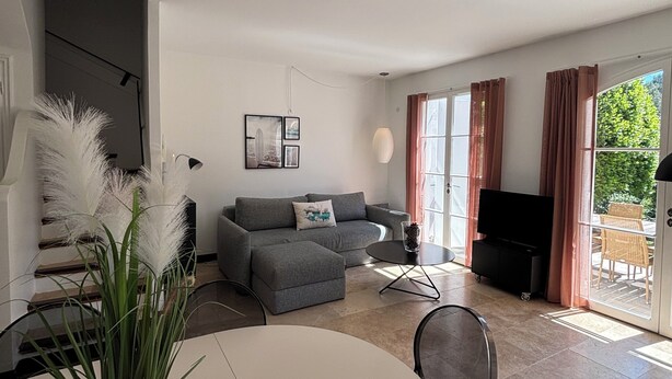 Een moderne woonkamer met een grijze bank, een eettafel en een televisie.