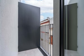 A balcony with a metal railing, a closed door, and a view of a building with a red roof. - Comfort & Light in Central Porto by HostWise (Porto)