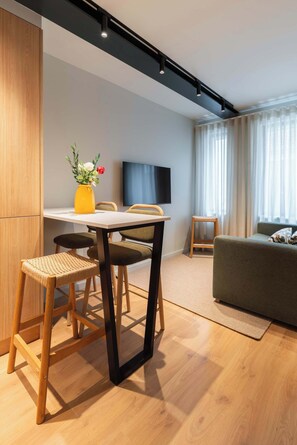 A modern living room with a dining area, wooden flooring, a sofa, a TV, and a small table with a yellow vase. - Comfort & Light in Central Porto by HostWise (Porto)