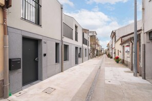 Una calle estrecha en la ciudad con edificios modernos, cielo despejado y una senda peatonal.