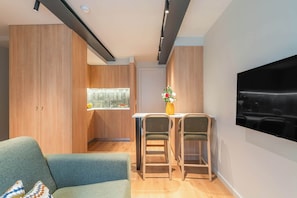 Una sala moderna con sofá, comedor para dos personas, televisor montado en la pared y cocina con armarios de madera.