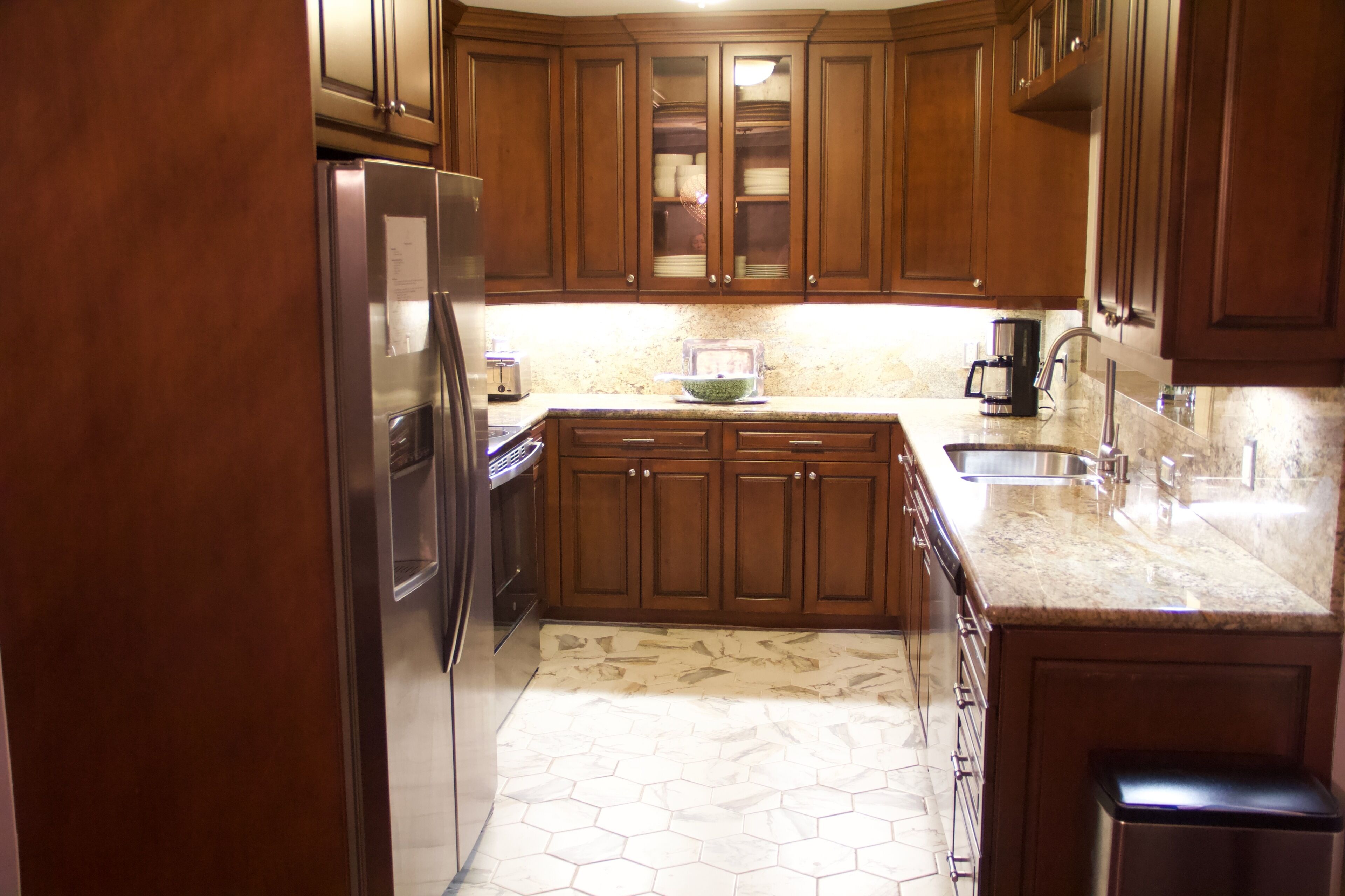 A kitchen with wooden cabinets, a stainless steel refrigerator, a granite countertop, a sink, and a coffee maker.