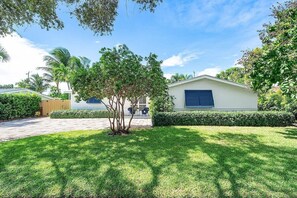 A well-maintained lawn, a building with a blue window, and a tree in the foreground. - Luxe Family Retreat with Heated Saltwater Pool — Steps to the Beach! (North Palm Beach)
