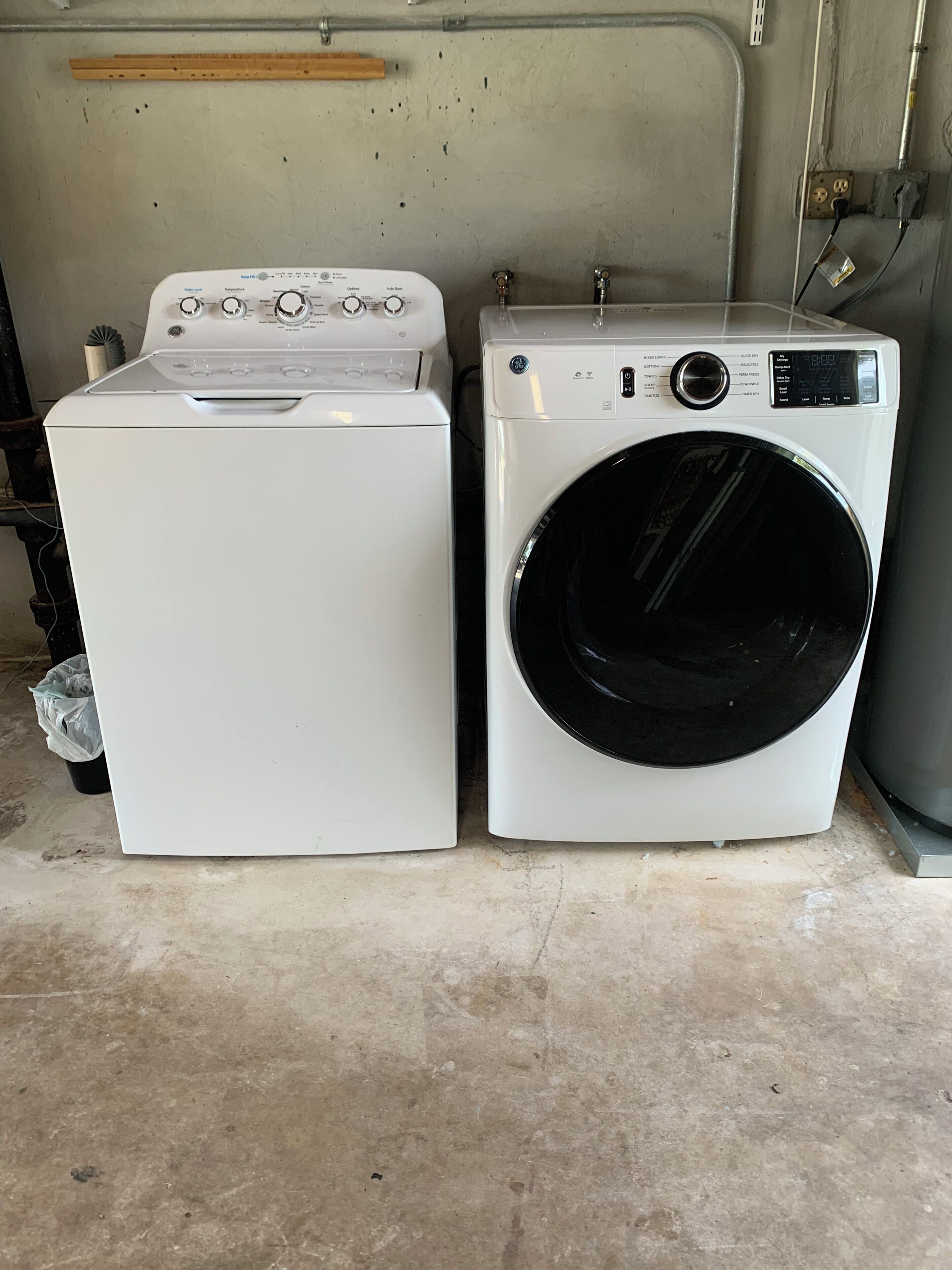 Two white washing machines side by side in a room with a concrete floor and a metal wall.