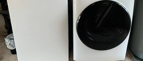 Two white washing machines side by side in a room with a concrete floor and a metal wall.