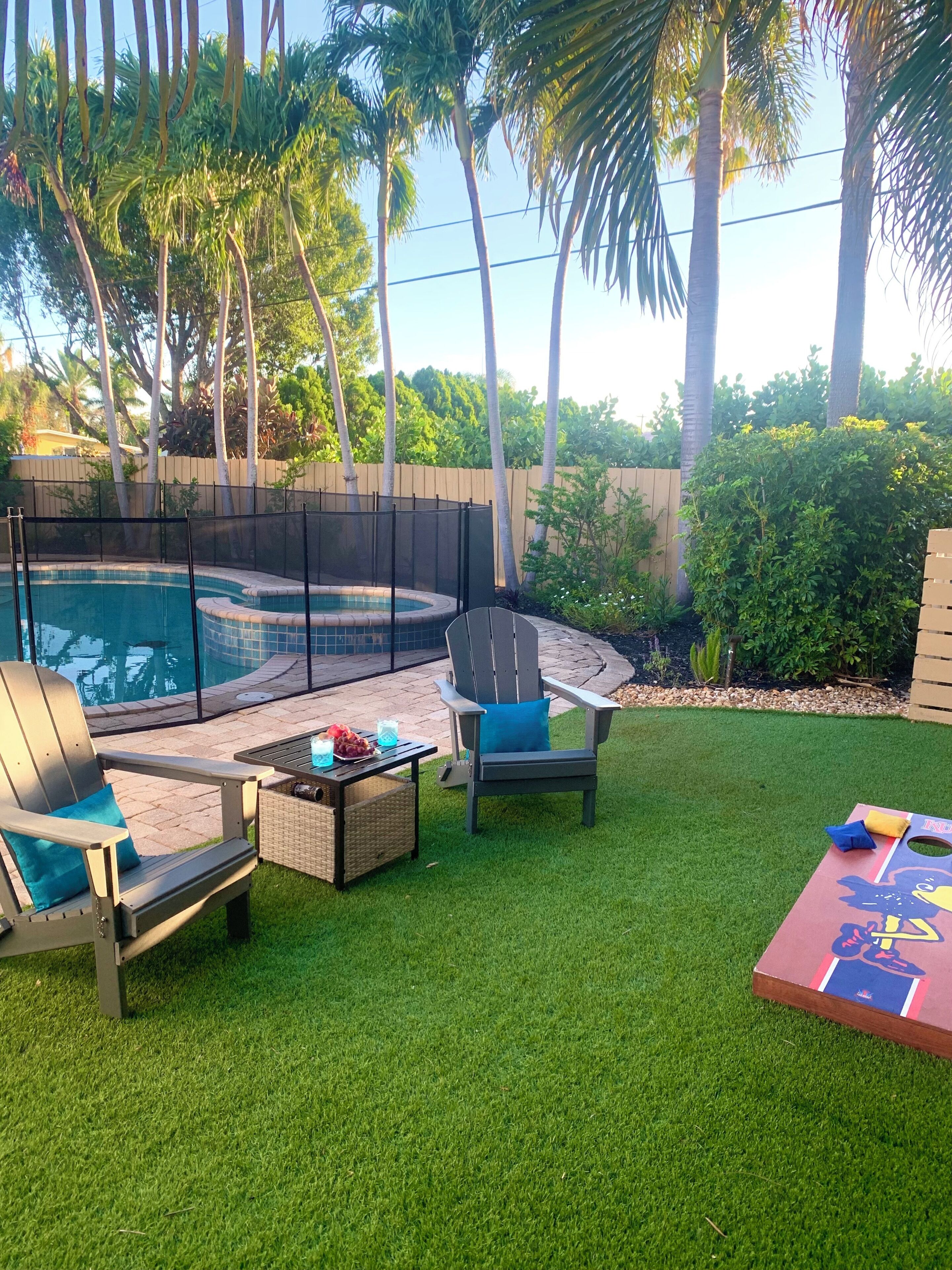 Un jardin avec une piscine, deux fauteuils Adirondack, une table avec des boissons et un espace de jeux pour enfants.