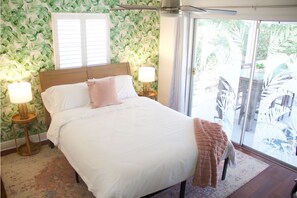 Une chambre à coucher avec un lit, deux lampes de chevet, une fenêtre et une vue sur le mobilier d’extérieur.