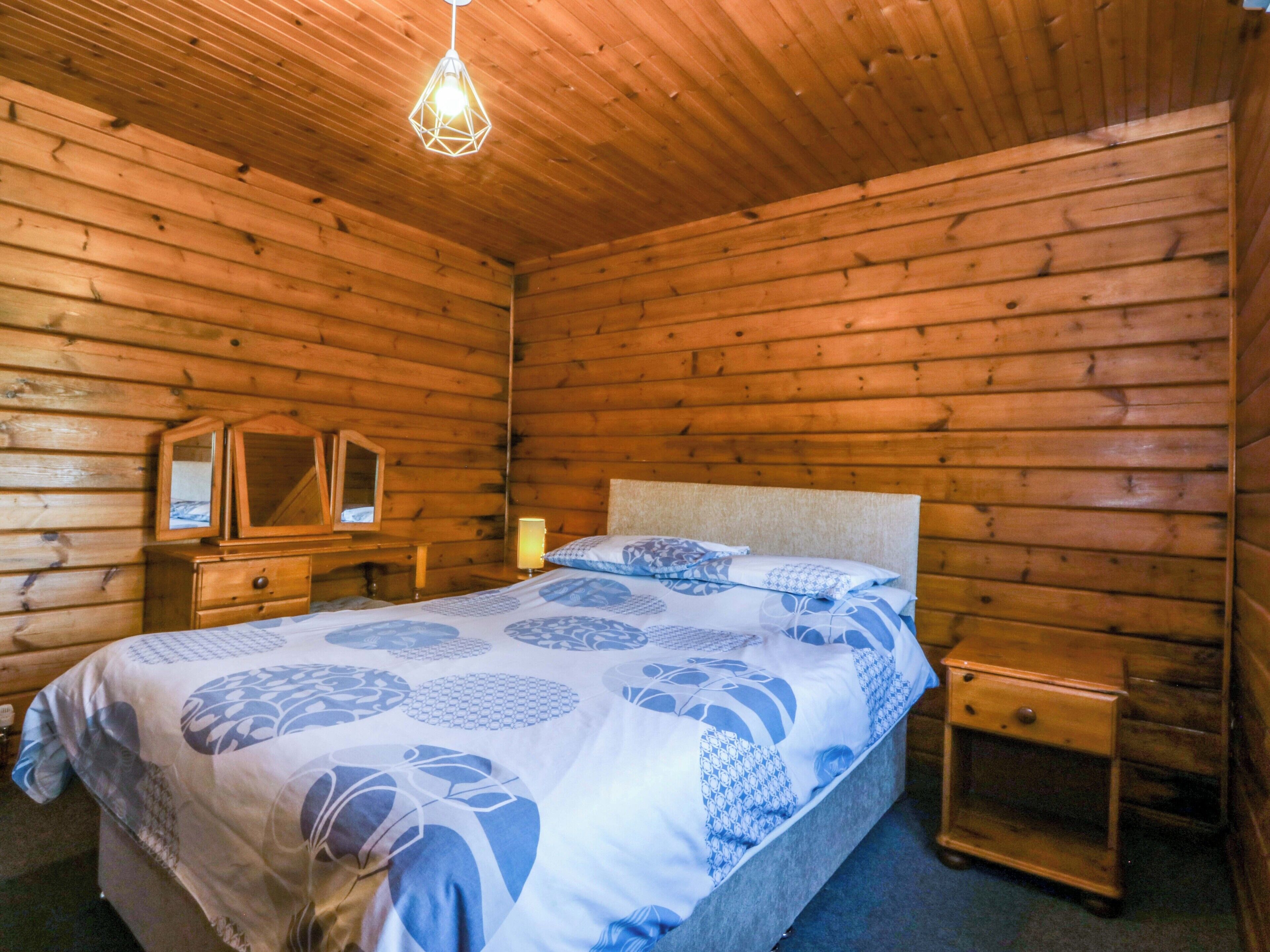 A wooden cabin bedroom with a bed, bedside table, and a hanging light fixture.