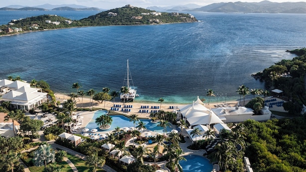 Un resort con una amplia piscina, zona de playa y un velero.