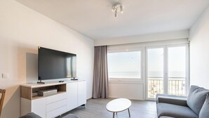 En moderne stue med et fladskærms-tv, en sofa, et lille bord og en balkon med udsigt.