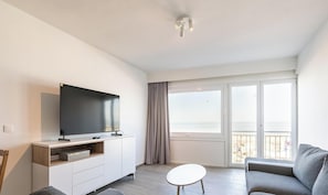 Ein modernes Wohnzimmer mit Flachbildfernseher, einer Couch, einem kleinen Tisch und einem Balkon mit Blick.