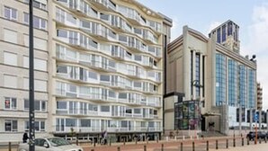 Et hotel med flere etager, altaner, en hovedindgang og parkeringsområde.