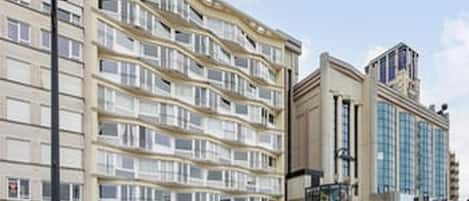 A multi-story hotel with balconies, a central entrance, and a parking area.