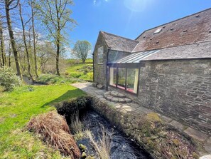 A stone building with a glass conservatory, a stone pathway, and a natural landscape with trees and a stream. - Historic Countryside Mill with Gardens/Tennis - Pass the Keys (Kirkpatrick Durham)