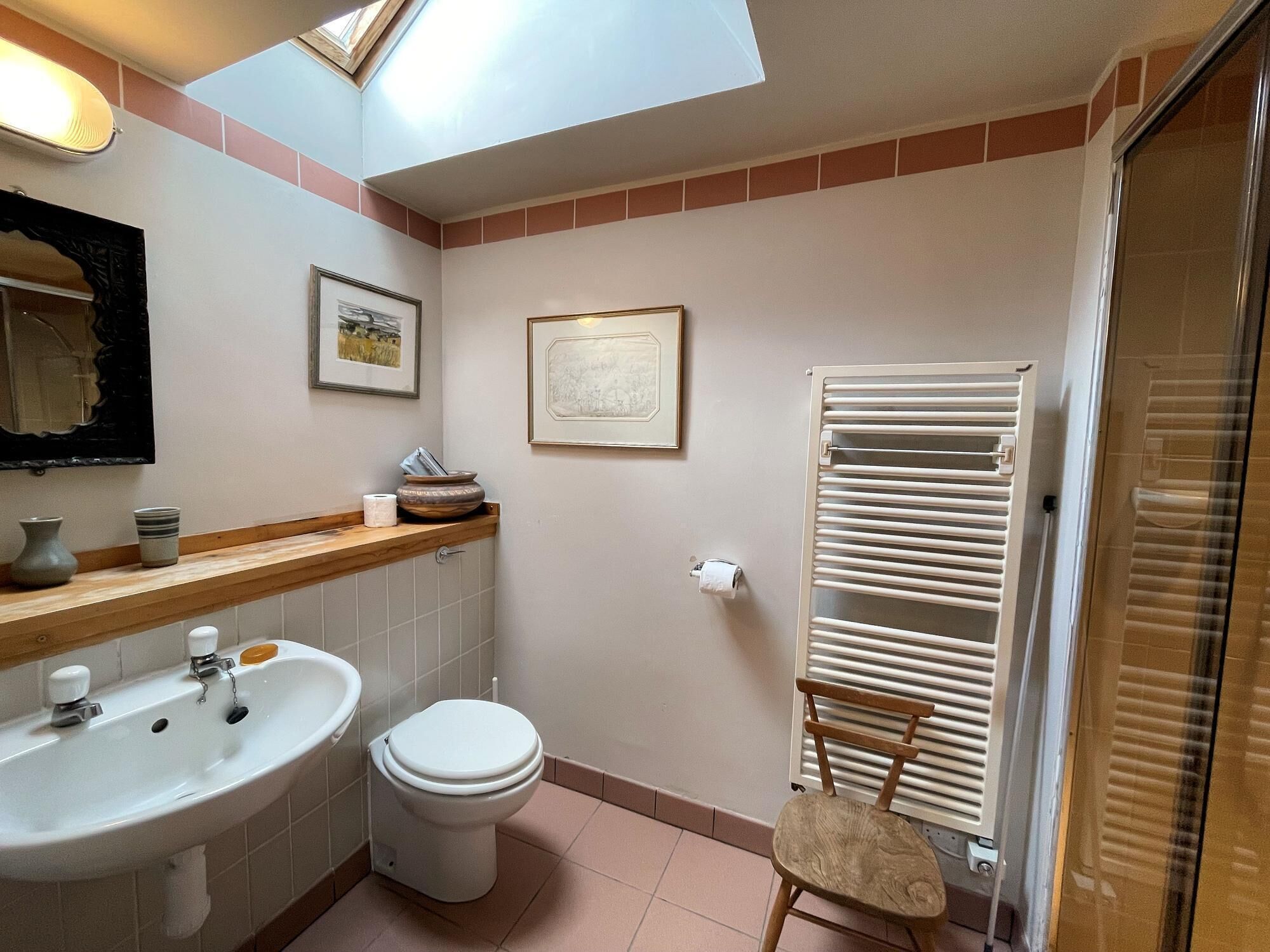 A bathroom with a sink, toilet, framed pictures, a towel rack, and a chair.