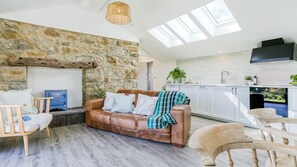 A modern living room with a stone wall, a leather sofa, and a wooden floor. - Pen Lon Quirt - sleeps 4 guests  in 2 bedrooms (Newborough)