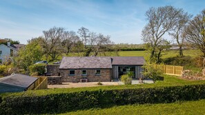 Ein Haus aus Stein mit einem geneigten Dach, einem eingezäunten Garten und einer Hecke im Vordergrund.