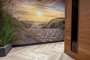 Ein Zimmer mit Fischgrätparkett, einem Wandgemälde mit Strandmotiv und einer Holztür.