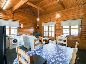 A cabin interior with a dining table, chairs, a washing machine, a television, and wooden walls. - Lodge 2 - Bron Eifion (Criccieth)