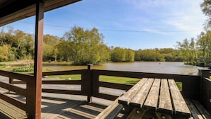 A wooden deck with a picnic table overlooking a river. - Lodge 2 - Bron Eifion (Criccieth)