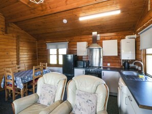 A cozy cabin with a dining table, two leather chairs, a refrigerator, a stove, and a sink. - Lodge 4 - Bron Eifion (Criccieth)