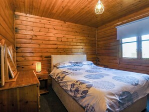 A wooden cabin bedroom with a bed, bedside table, lamp, and window. - Lodge 4 - Bron Eifion (Criccieth)
