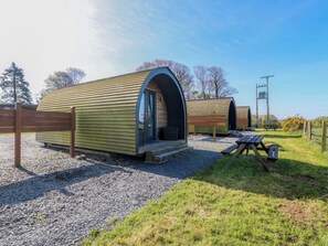 A row of wooden pod-style accommodations with a gravel ground, a picnic table, and a wooden fence. - Bron Eifion Pod 2 (Criccieth)