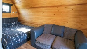 A cozy room with a sloped ceiling, a bed with floral bedding, a sofa with cushions, and a window. - Bron Eifion Pod 2 (Criccieth)