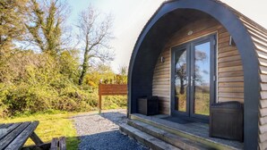 A small, modern cabin with a curved roof, a wooden deck, and a bench. - Bron Eifion Pod 2 (Criccieth)