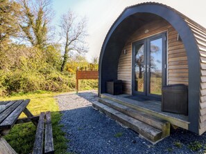 A small, modern cabin with a curved roof, a wooden deck, and a bench. - Bron Eifion Pod 2 (Criccieth)
