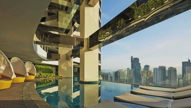 A rooftop infinity pool with lounge chairs, a glass balustrade, and a city skyline view. - The Gramercy Residences-58th floor w/balcony+Skyline view (Makati)